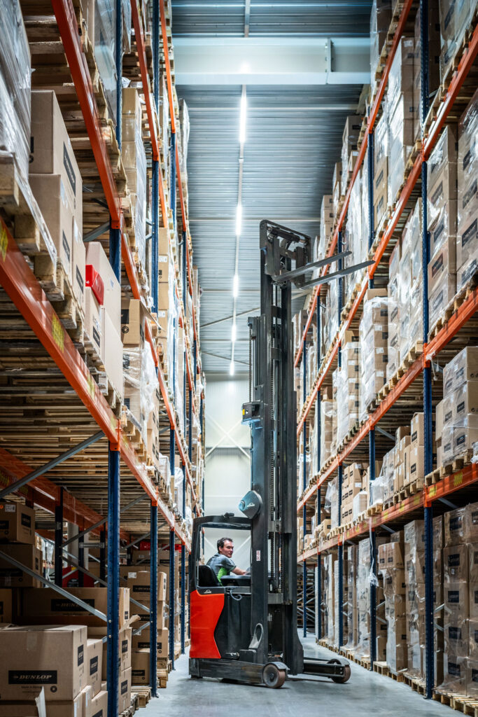 Medewerker op heftruck tussen stellingen in warehouse