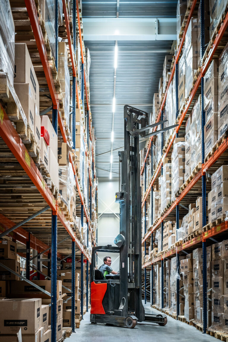Medewerker op heftruck tussen stellingen in warehouse
